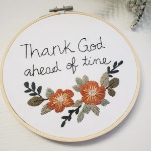 6 inch embroidery hoop with orange florals and the words "thank god ahead of time" in olive green lettering.