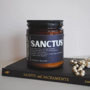 Sanctus Candle with rosary on top of Saints Sacraments books