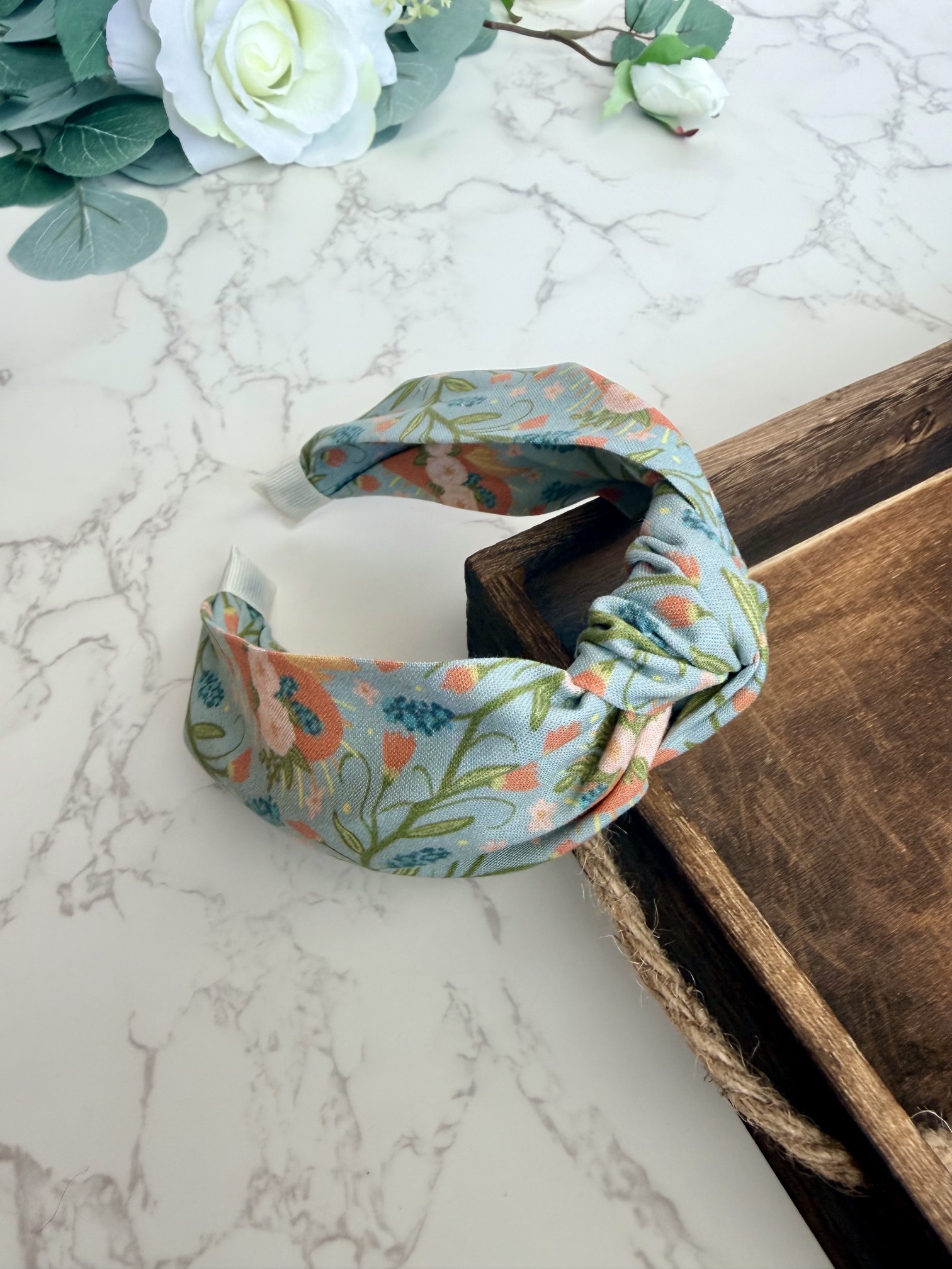 Knotted headband with images of the Immaculate Heart of Mary surrounded by a lovely floral pattern on a blue gray background.