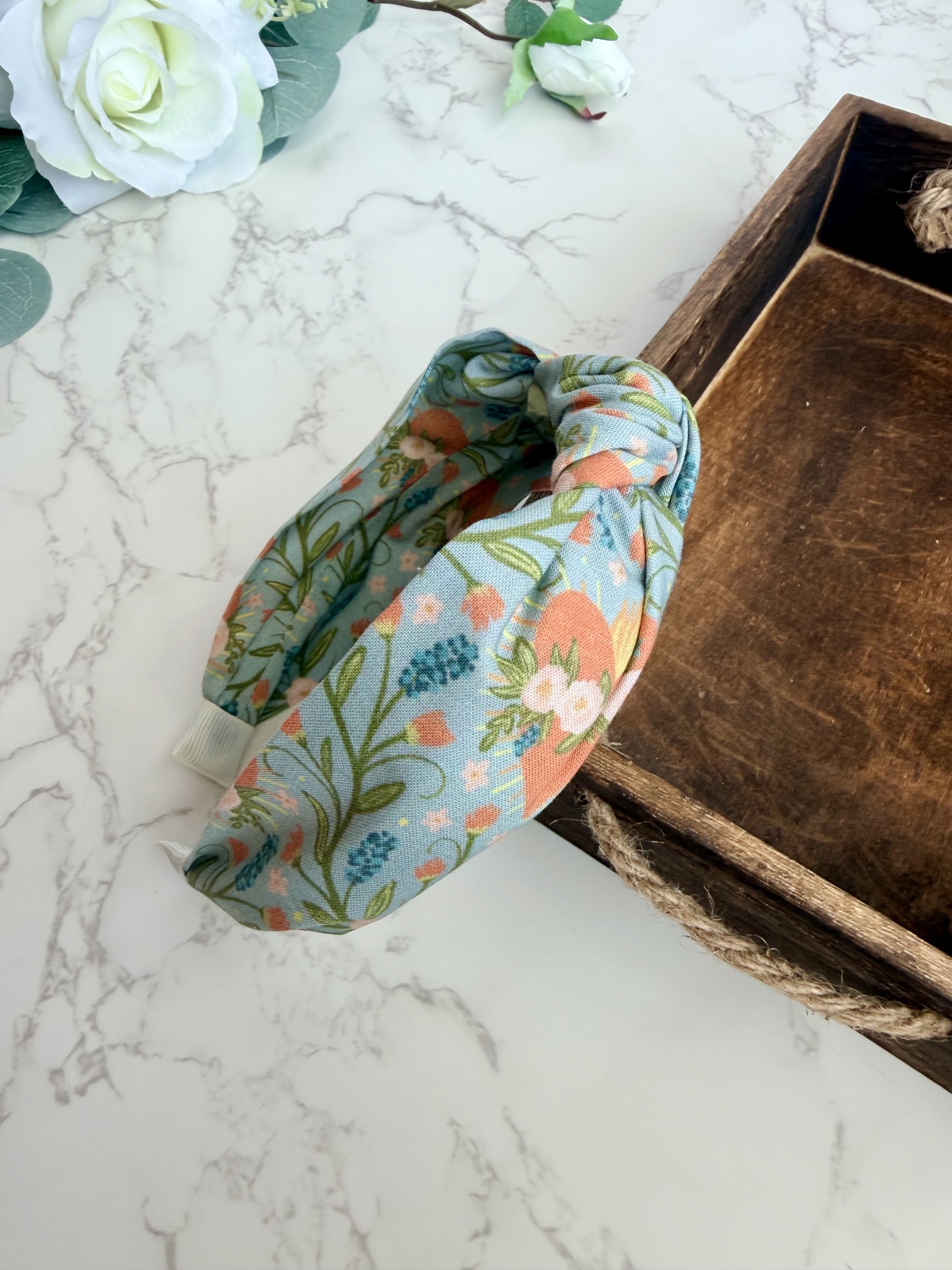 Knotted headband with images of the Immaculate Heart of Mary surrounded by a lovely floral pattern on a blue gray background.