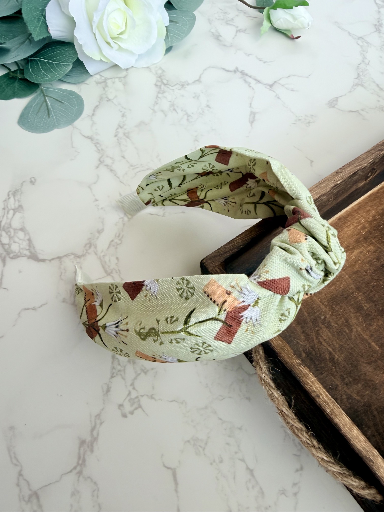 Light green knotted headband with images of carpenter square and lily.