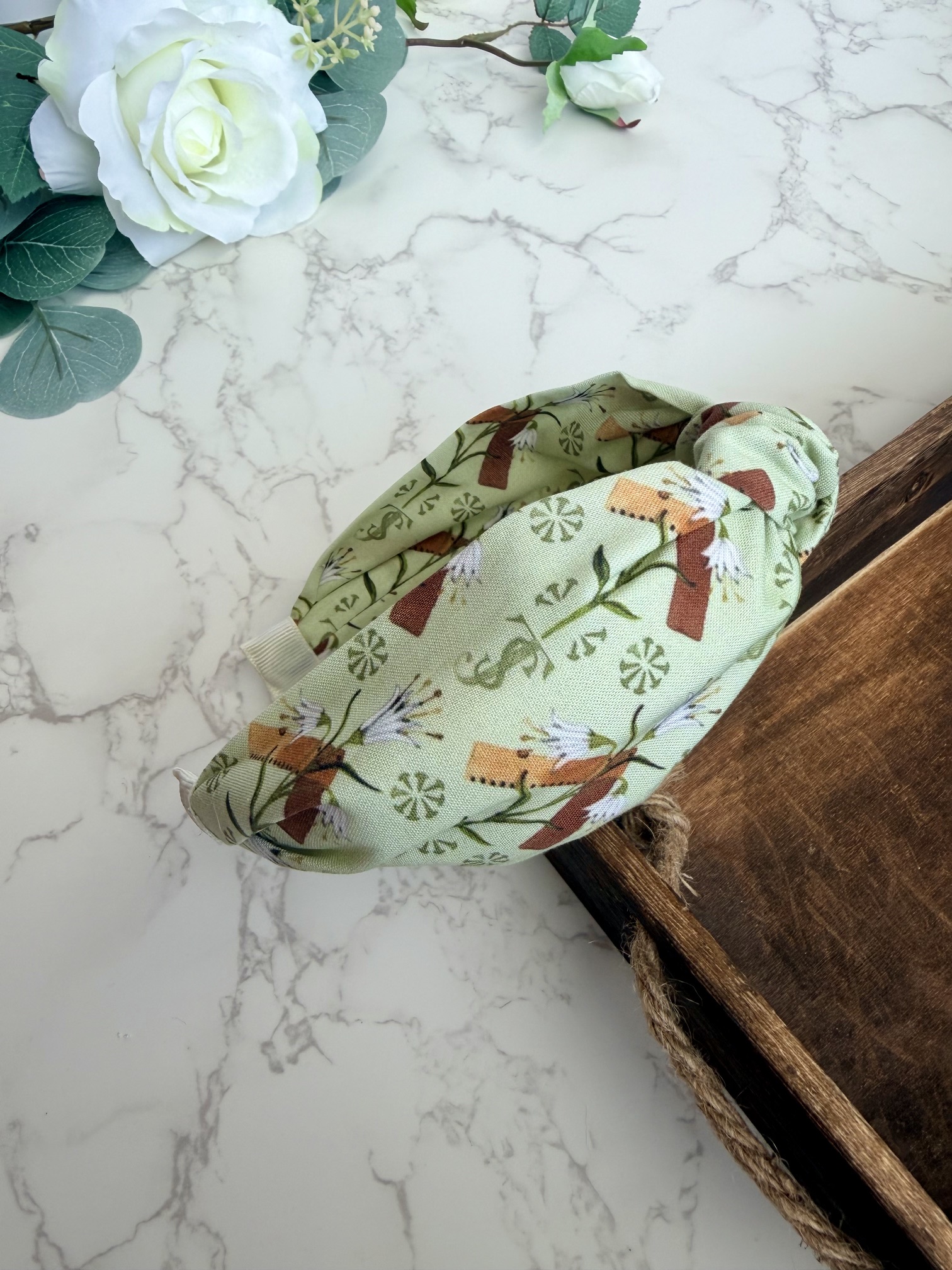 Light green knotted headband with images of carpenter square and lily.