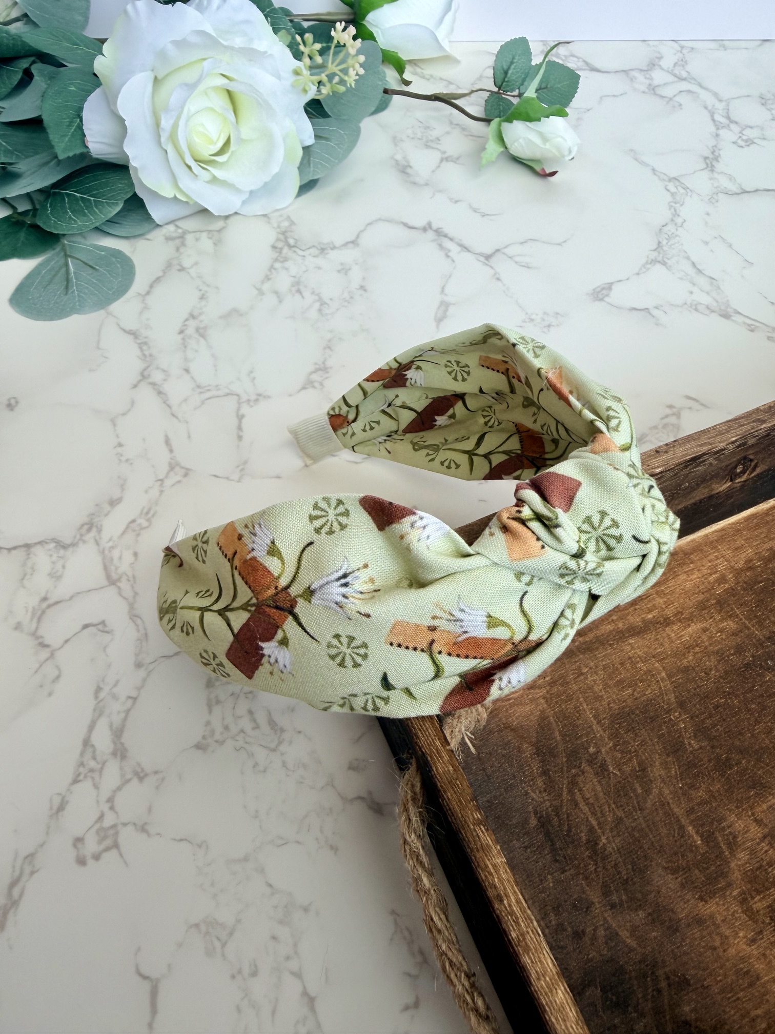 Light green knotted headband with images of carpenter square and lily.