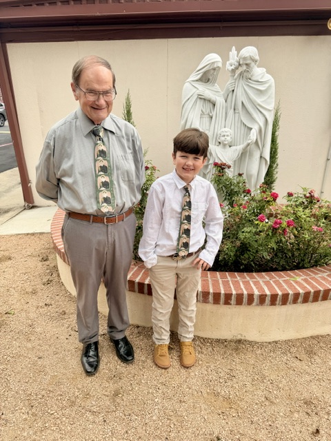 Grandpa and grandson wearing matching Fulton Sheen ties in front of the Holy Family.
